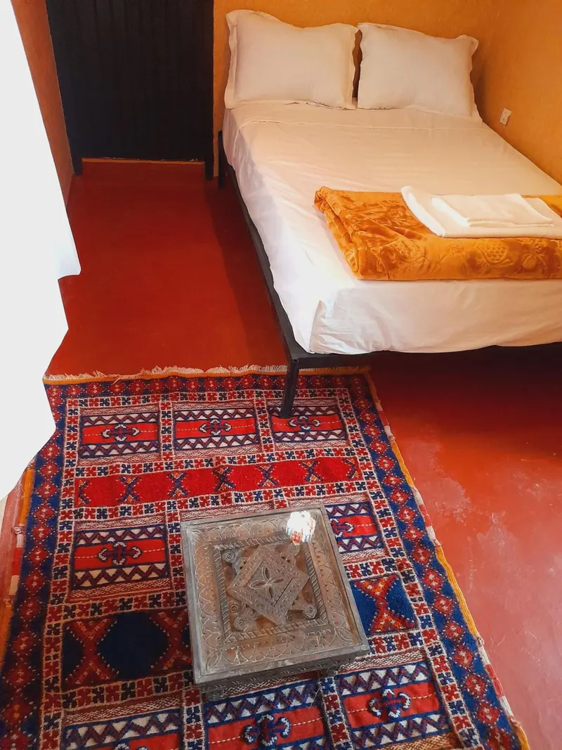 Double or Twin Room: the bed, a carved table and a red rug