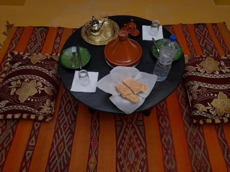 A tagine and bread on a round table over striped rugs